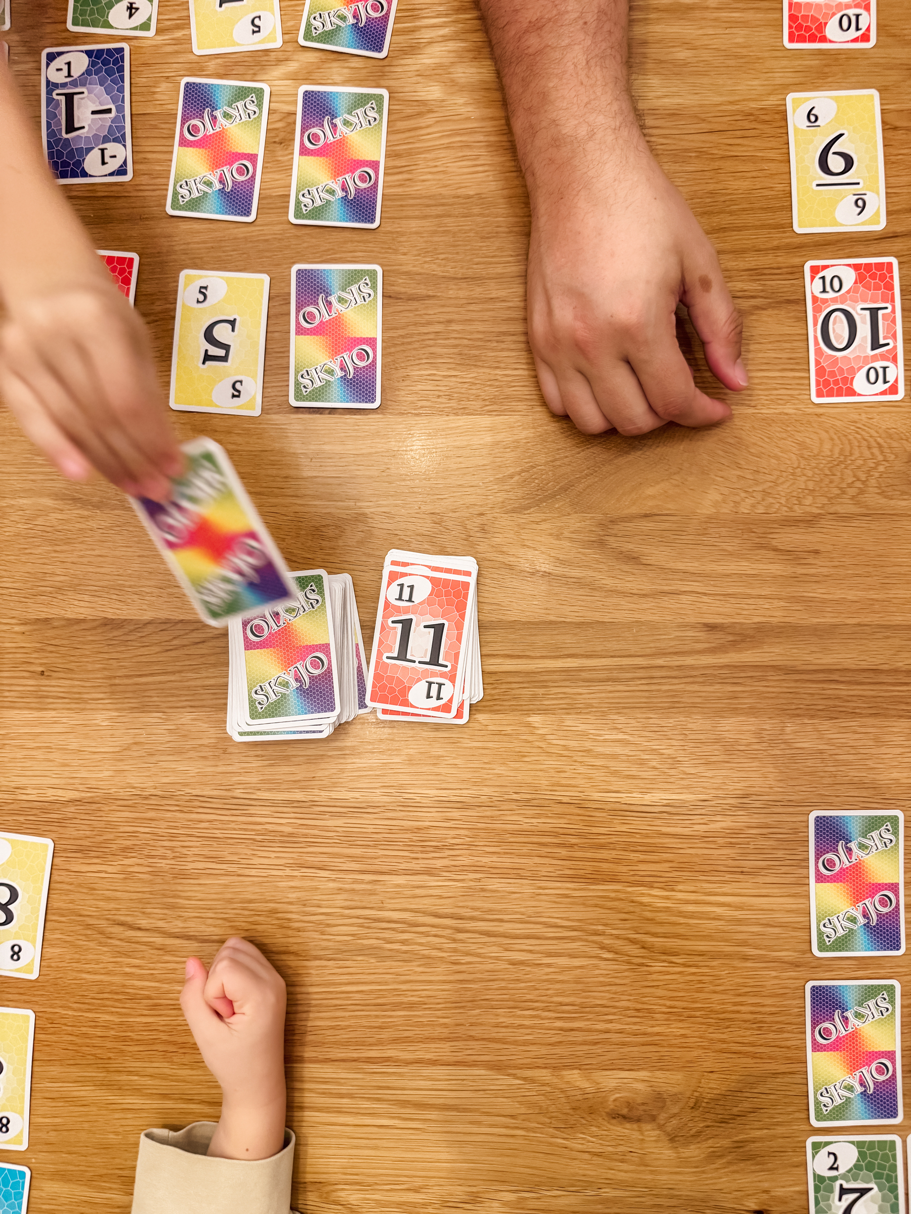 A family is playing a colorful card game at a wooden table.