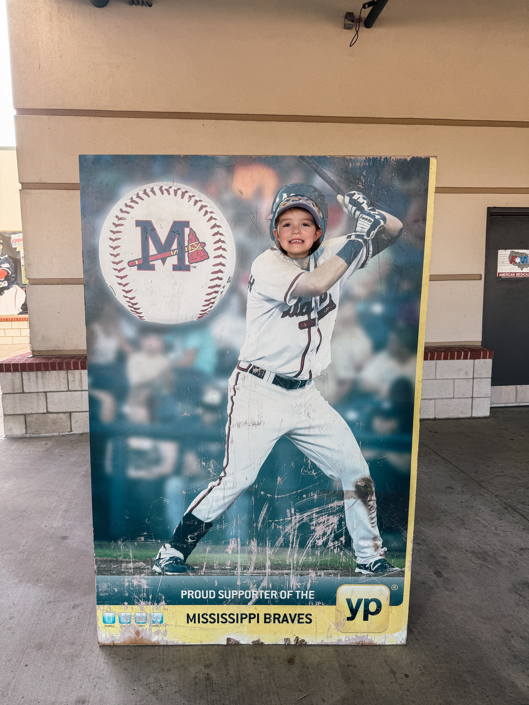 A young girl smiling through a photo cutout of a baseball player