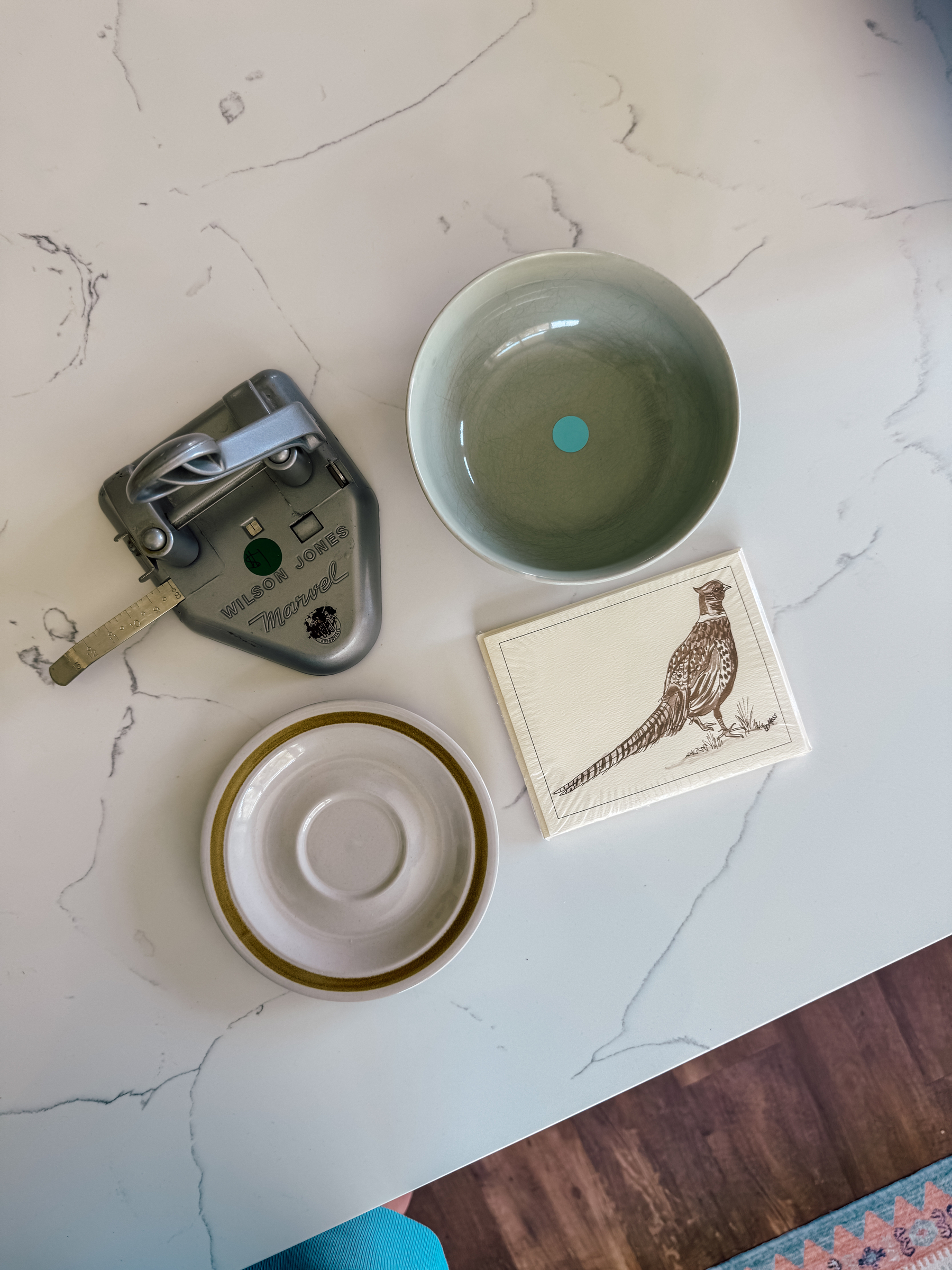 A 2-hole punch, a green ceramic bowl, a small plate, and a set of cards with a bird illustration are arranged on a quartz countertop