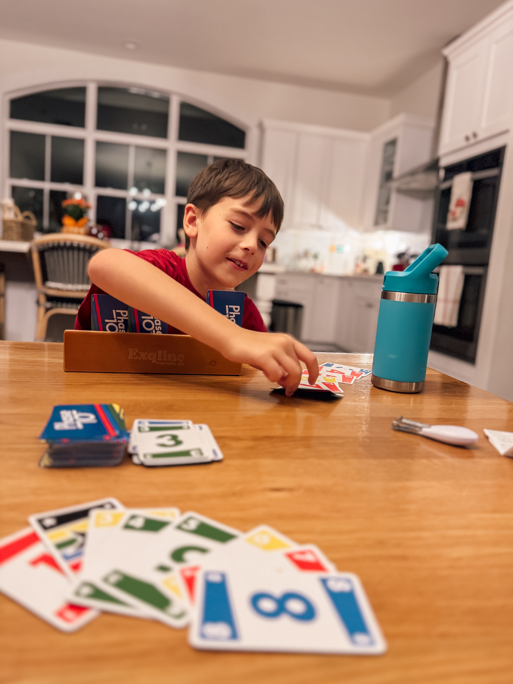 A child is playing a card game at a kitchen table with a blue water bottle nearby.