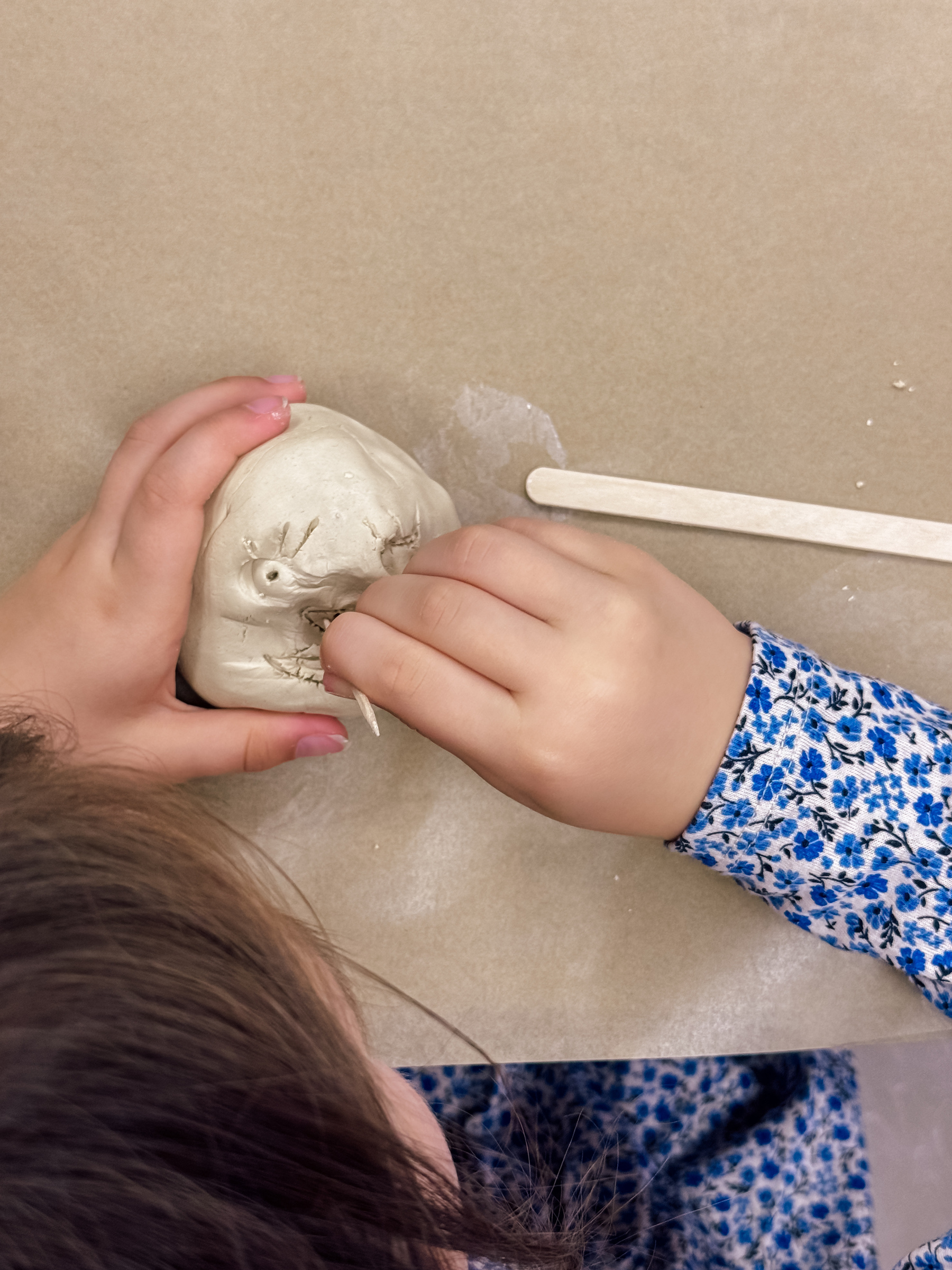 A child carving a face with a toothpick into clay shaped like a head