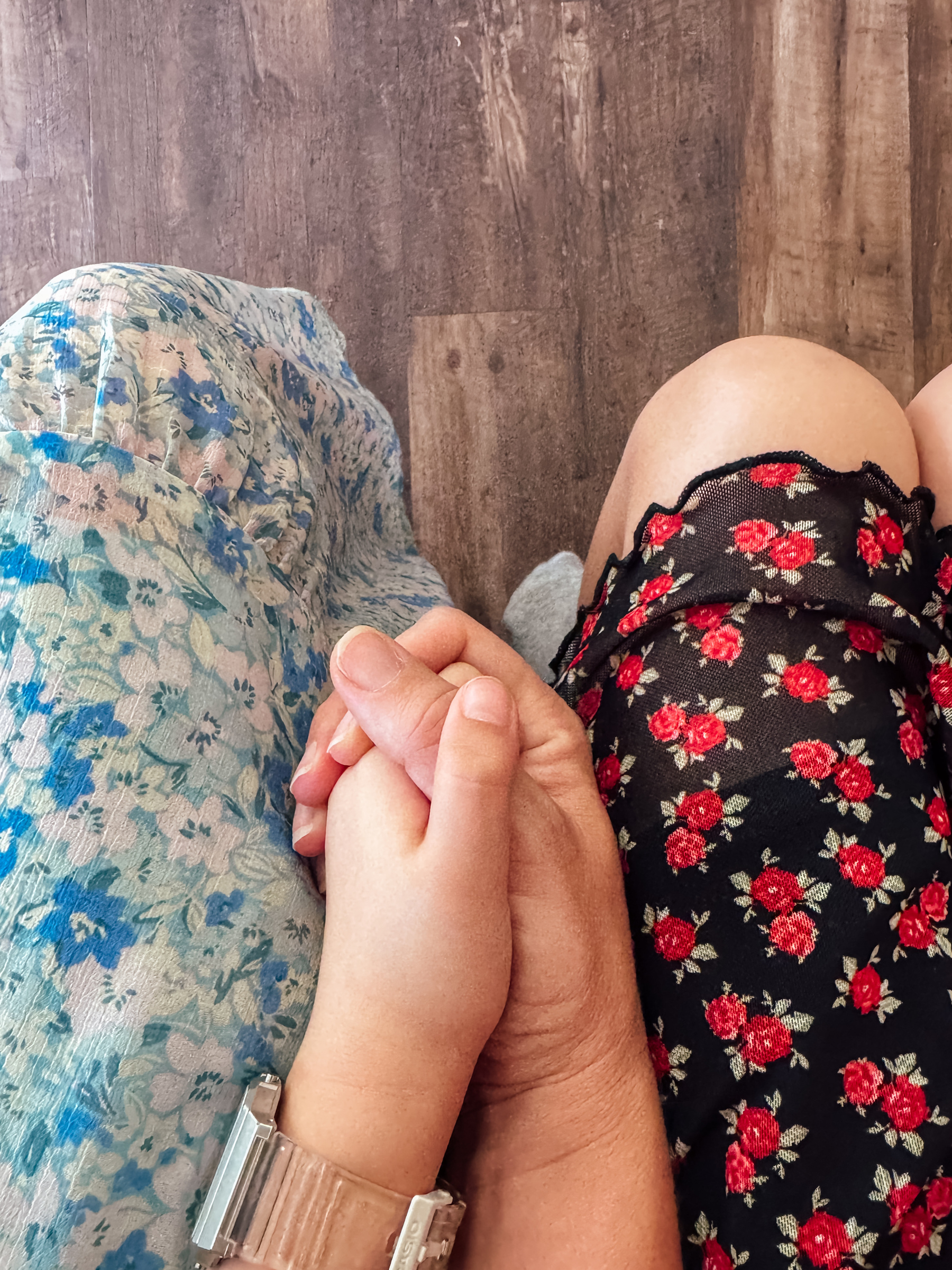 A child and an adult are holding hands while sitting, wearing floral-patterned outfits.