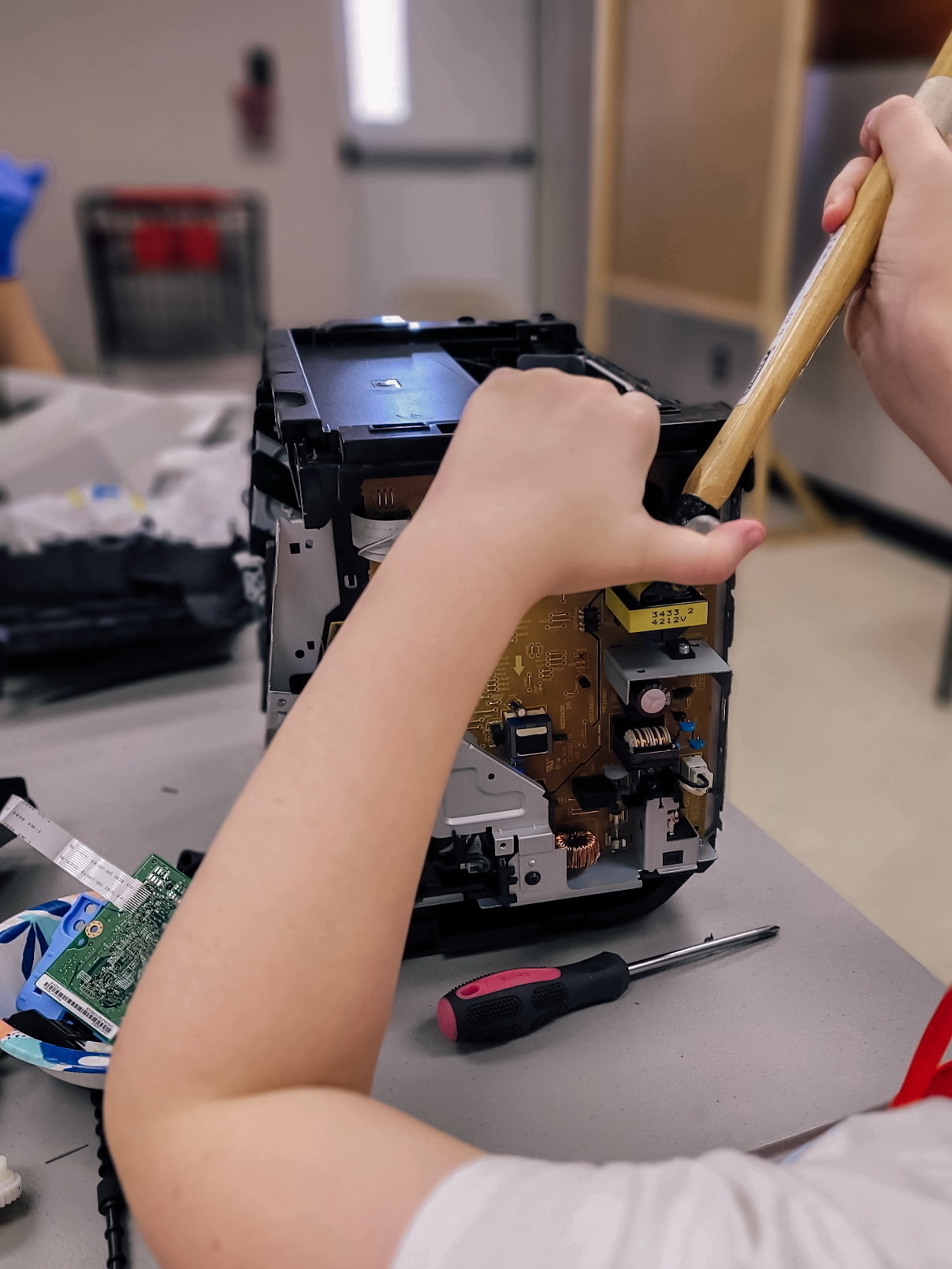 Auto-generated description: A person is using a tool to disassemble a piece of electronic equipment on a table, with a screwdriver and circuit boards nearby.