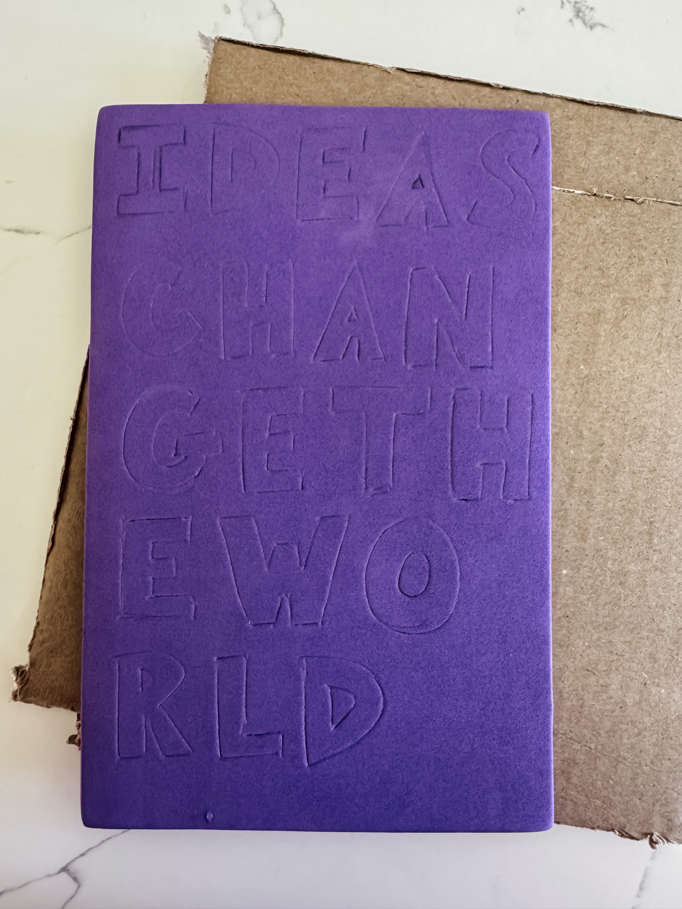Auto-generated description: A purple notebook cover displays the embossed words IDEAS CHANGE THE WORLD.