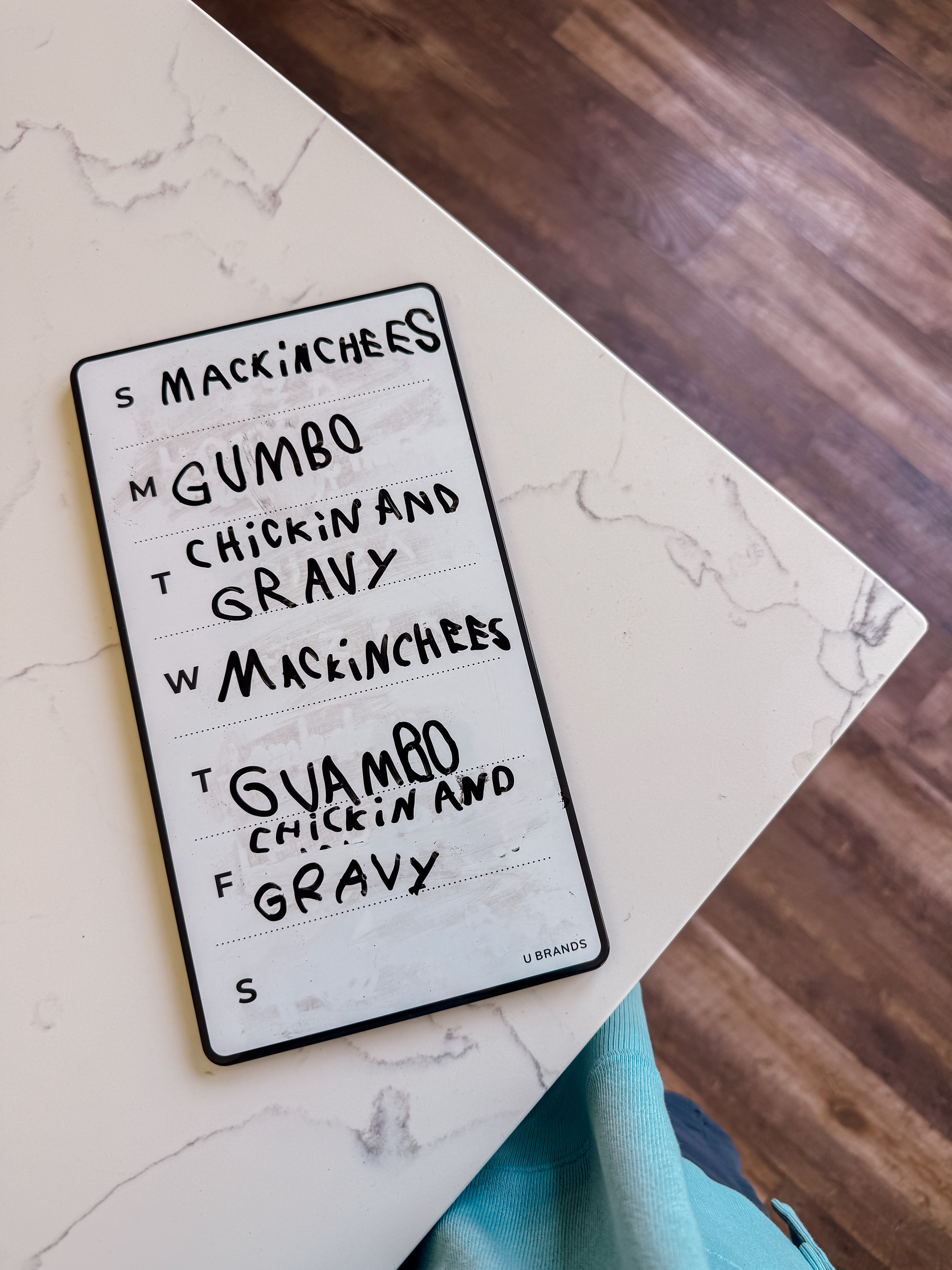 A weekly meal planner on a countertop lists dishes like Mac 'n' Cheese and Gumbo for each day.
