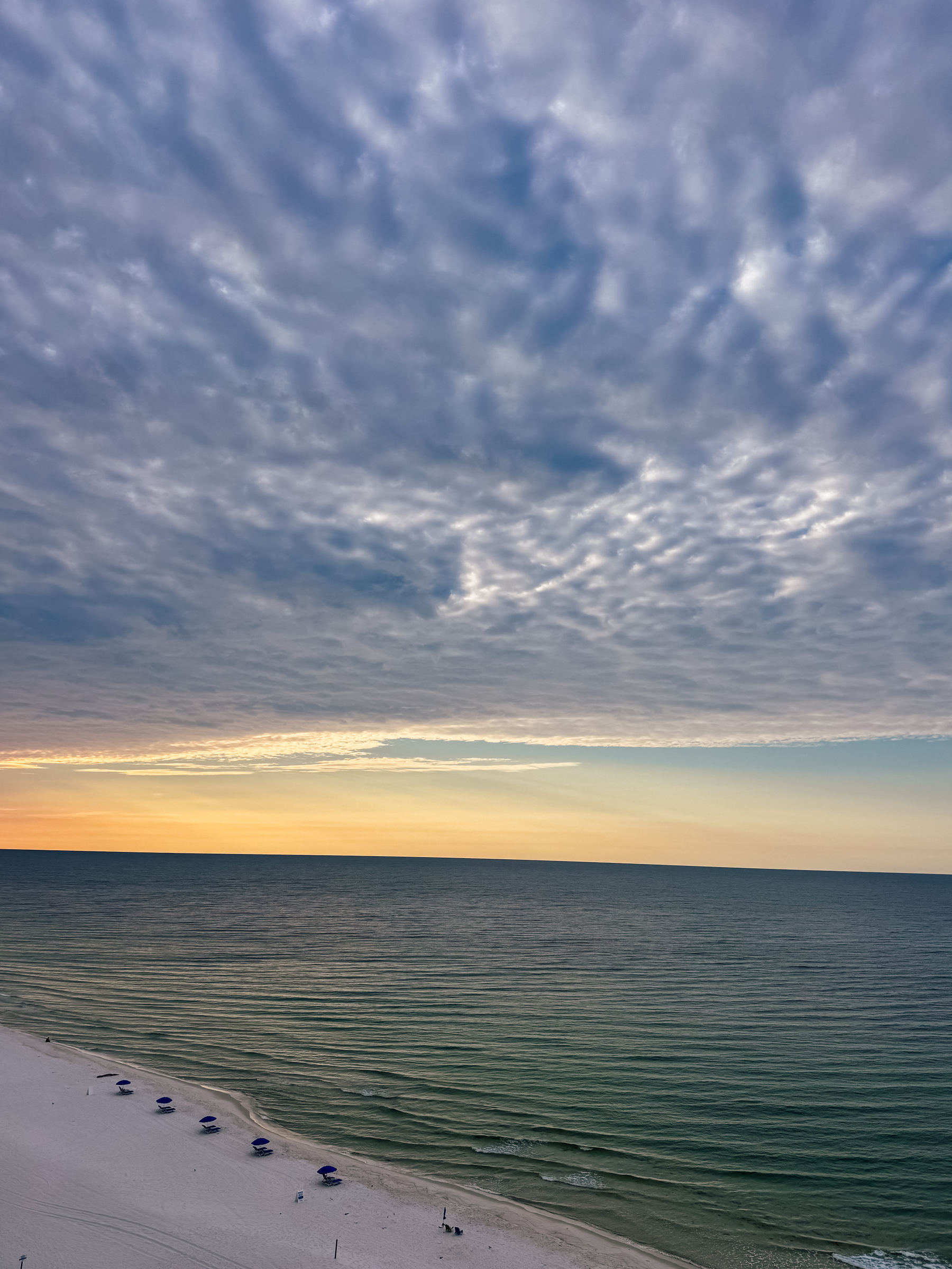 A serene beach scene shows a vast ocean under a dramatic, cloud-filled sky at sunrise.