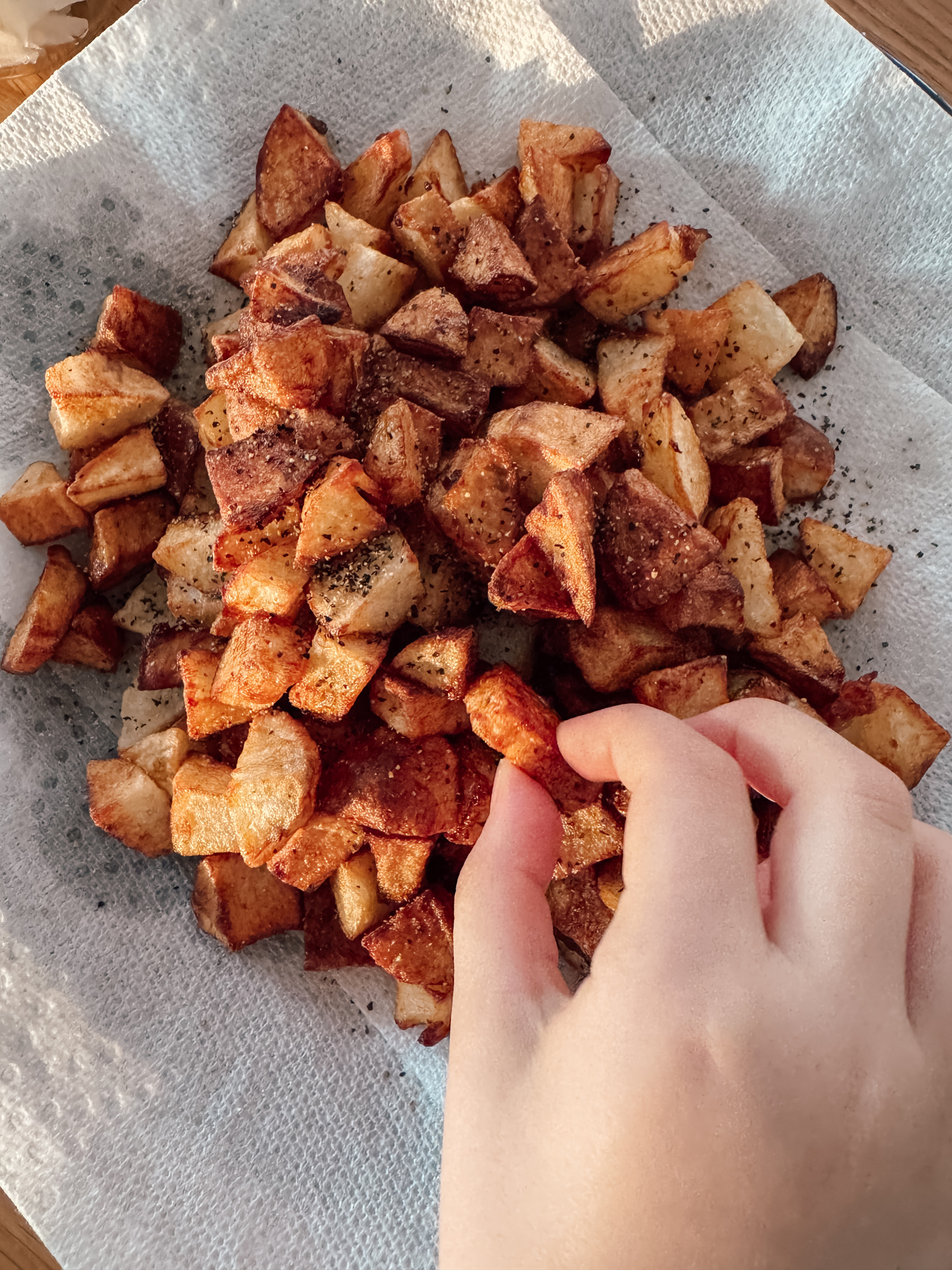 A hand reaches for a pile of seasoned, cubed potatoes on a paper towel.