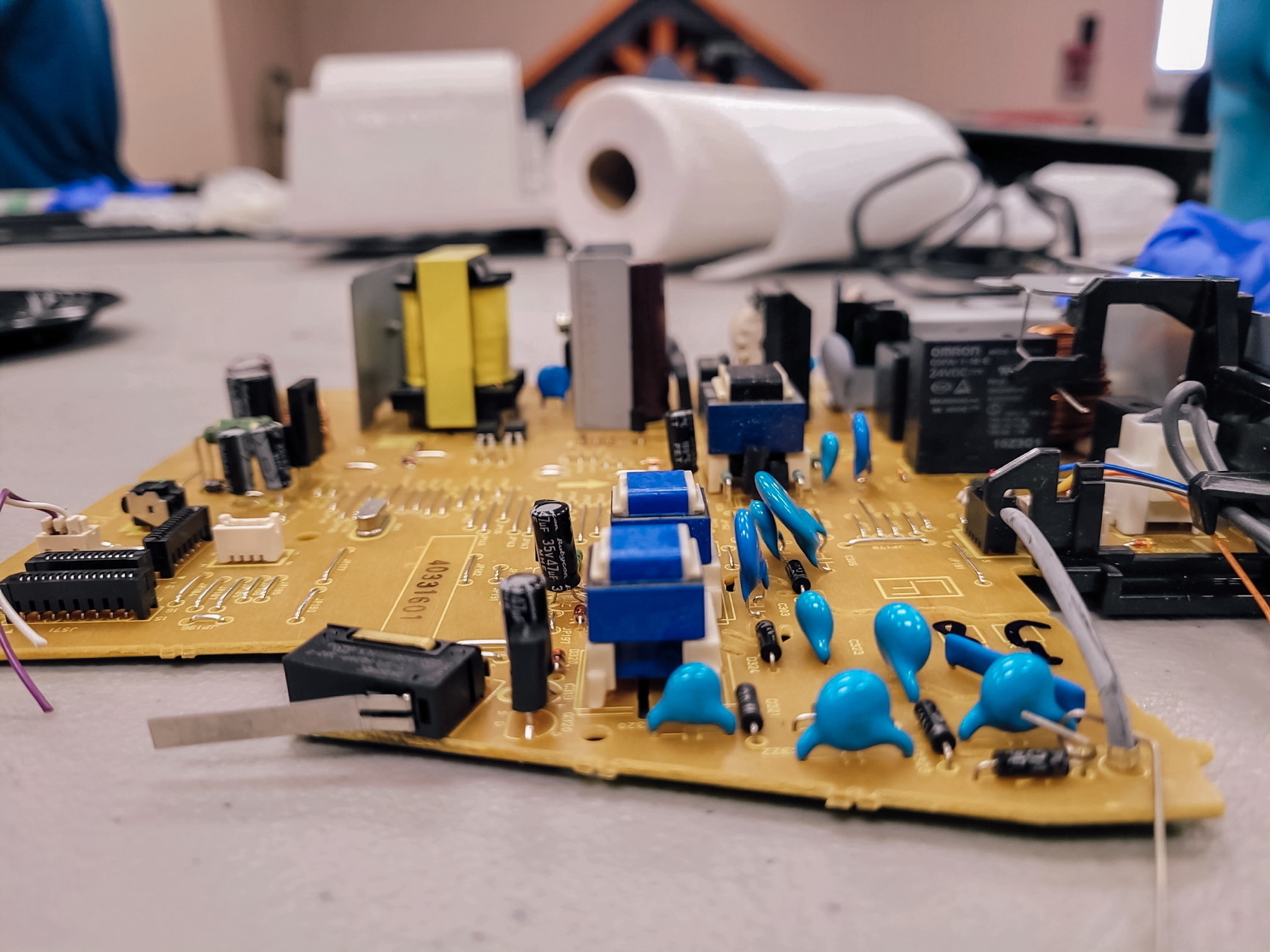 Auto-generated description: A circuit board with various electronic components, including blue capacitors and connectors, is placed on a table.