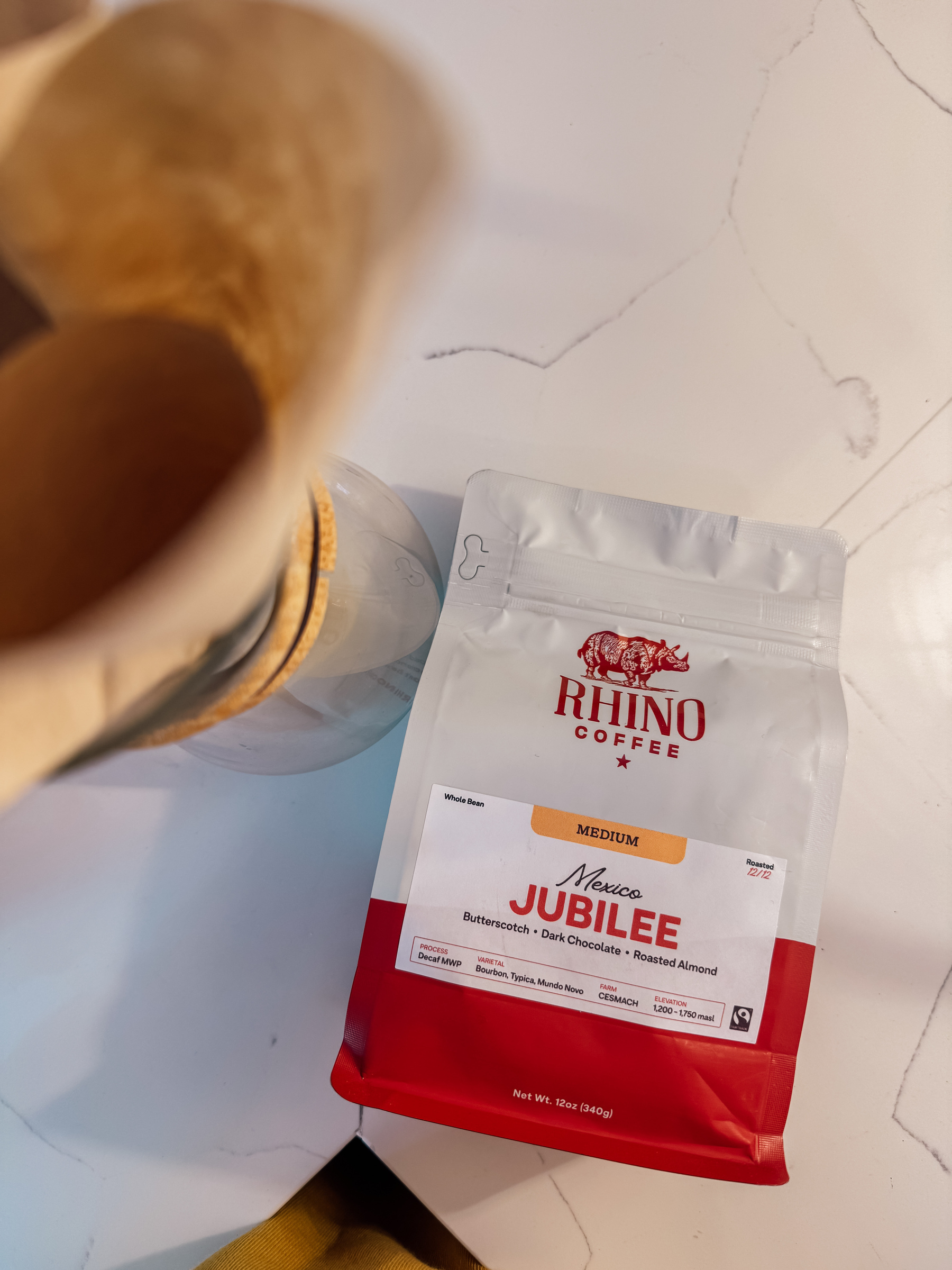 A bag of Rhino Coffee labeled "Jubilee" is on a marble surface next to a Chemex coffee maker.