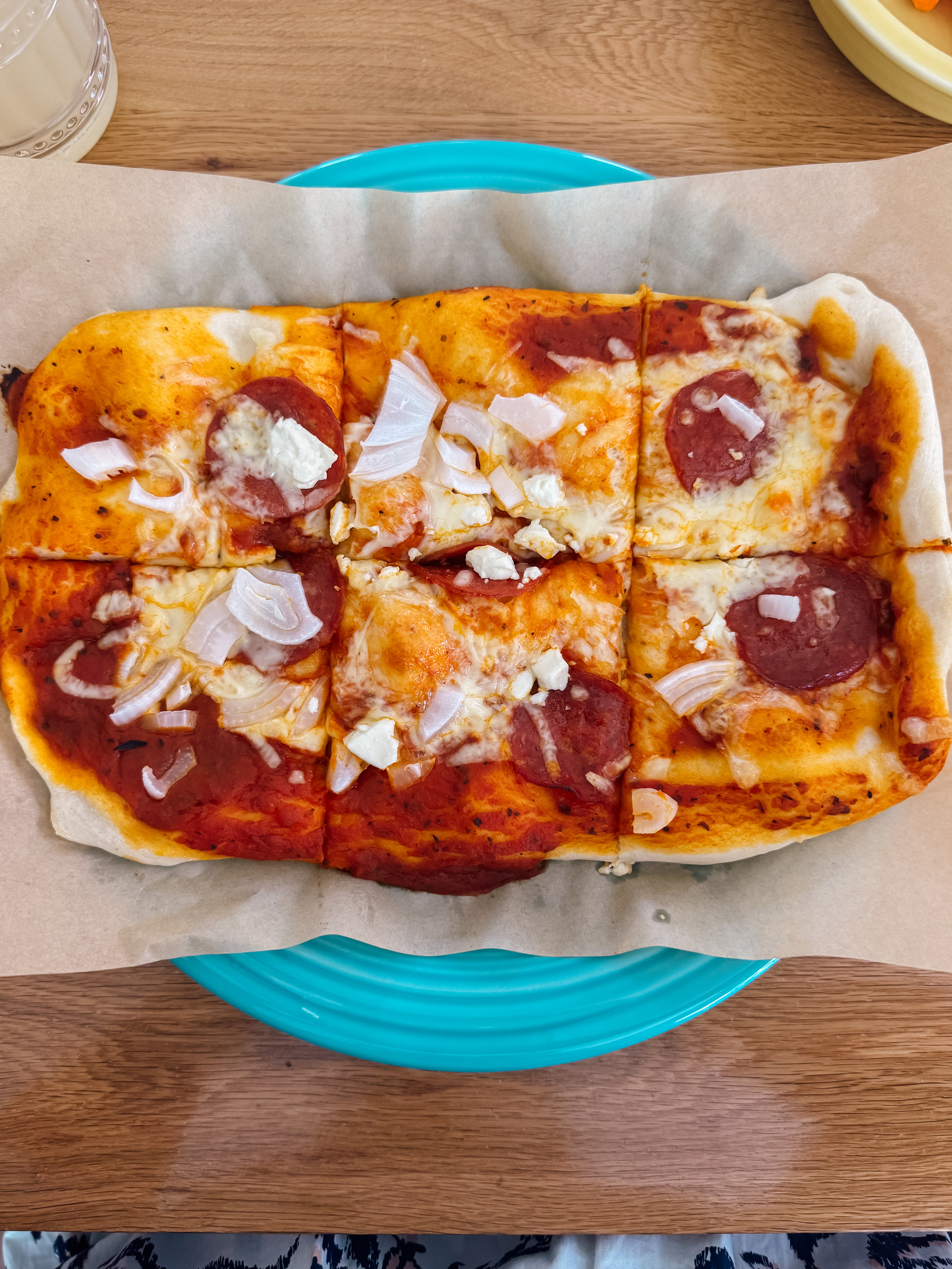 A rectangular pizza topped with tomato sauce, cheese, pepperoni, and chopped onions is placed on parchment paper over a blue plate.