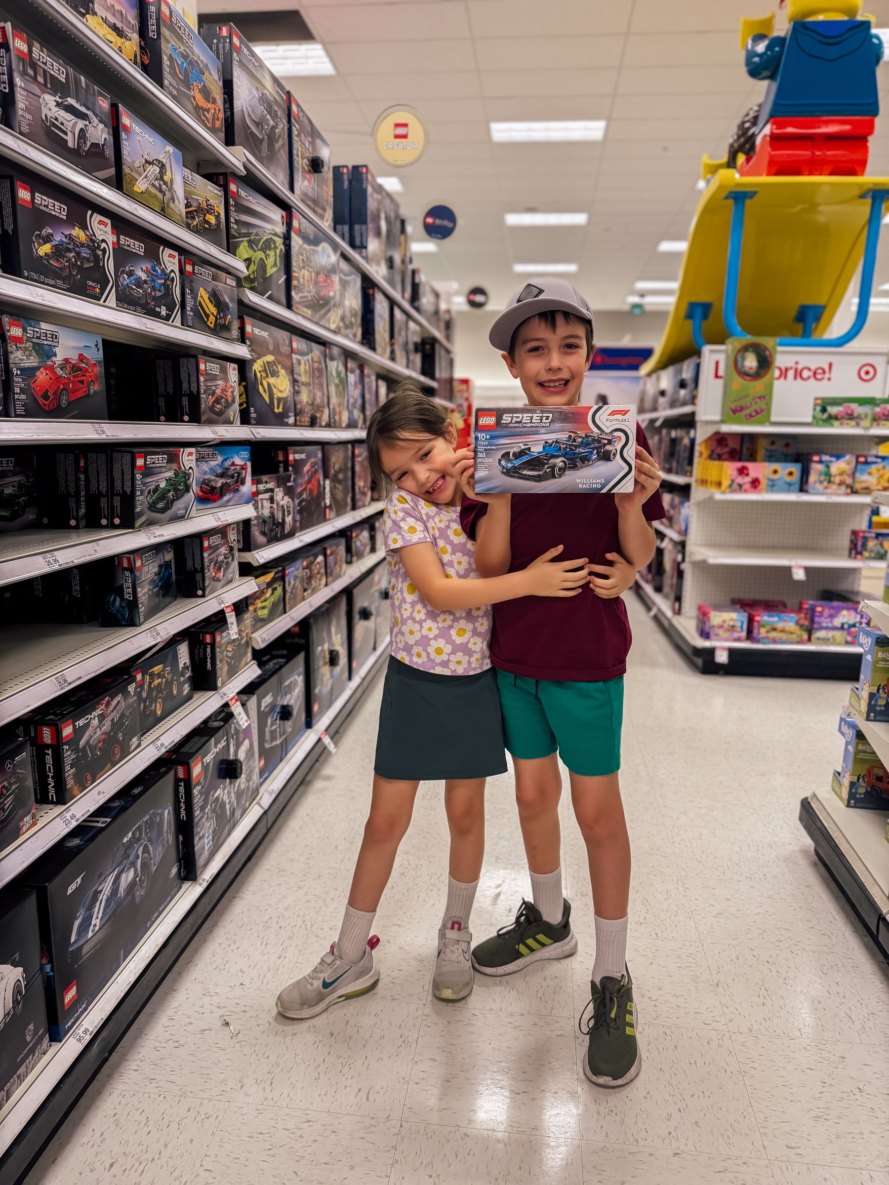 Two children happily holding a LEGO set in a toy store aisle.