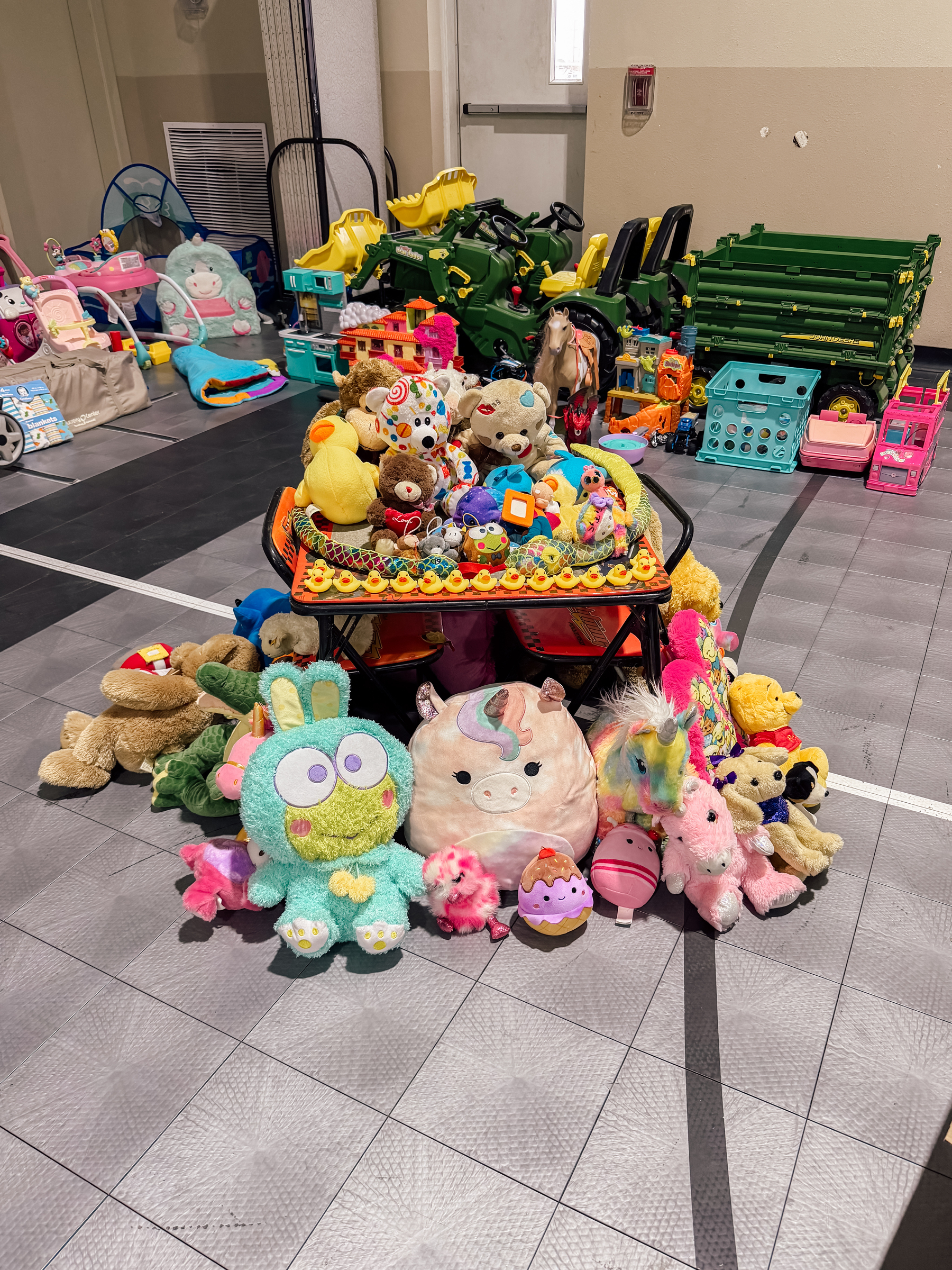 A collection of colorful stuffed animals and toys is displayed on a gym floor.